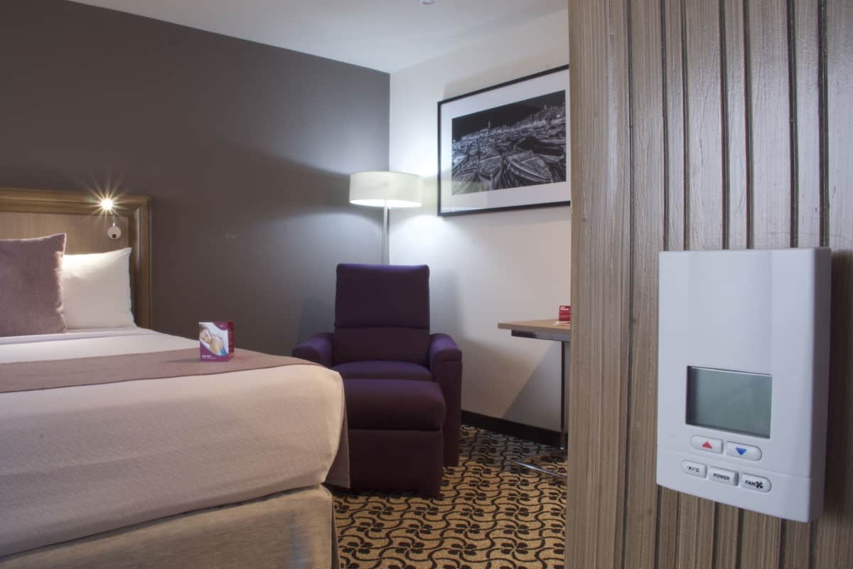 Una habitación de hotel con una cama, un sillón púrpura, un escritorio y un termostato.