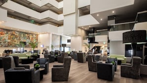 A spacious lobby with multiple seating areas, a large mural on the wall, and a modern staircase.