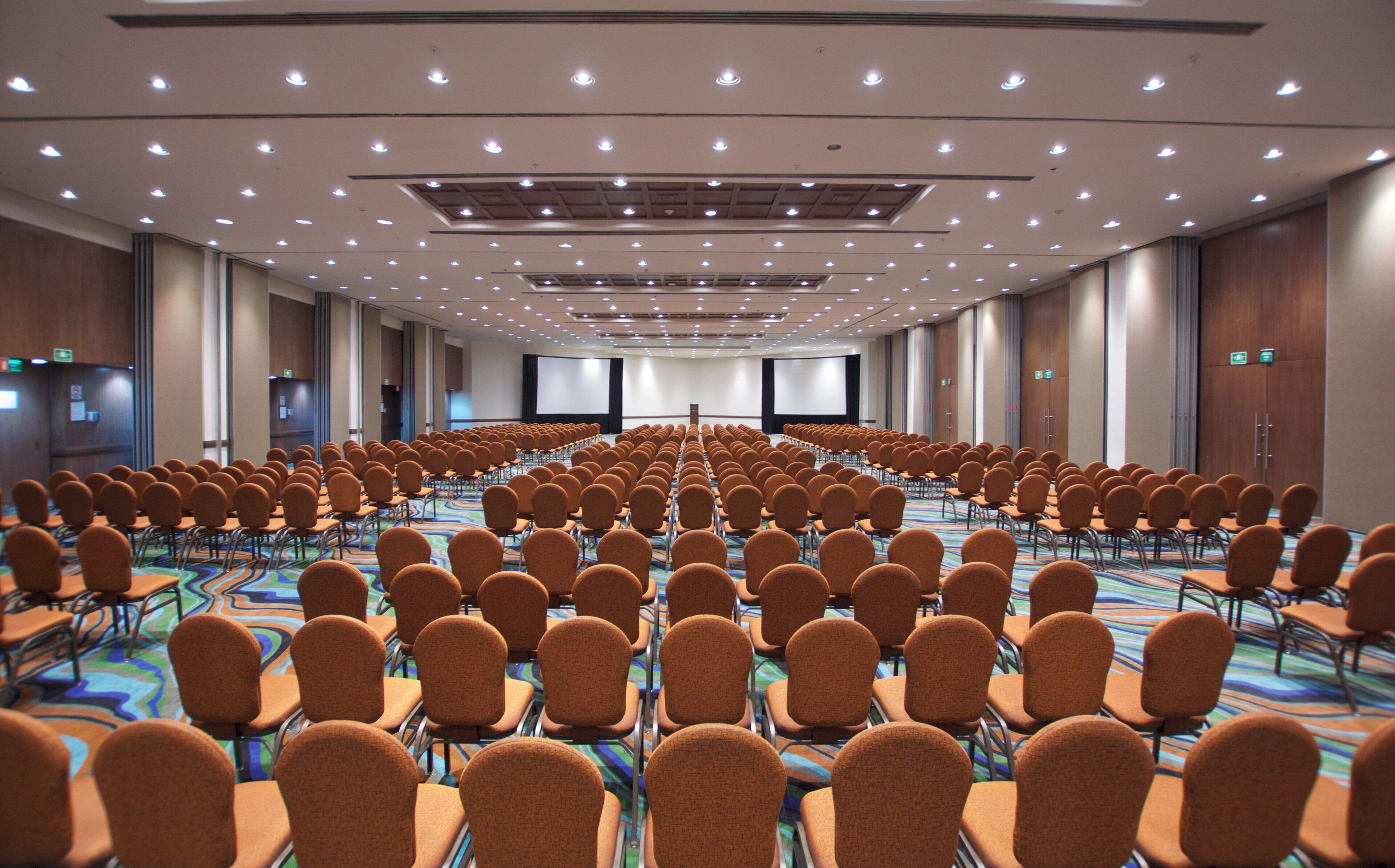 A conference room with rows of chairs and a large screen at the front.