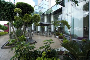 An outdoor seating area with tables and chairs, surrounded by various plants and trees.