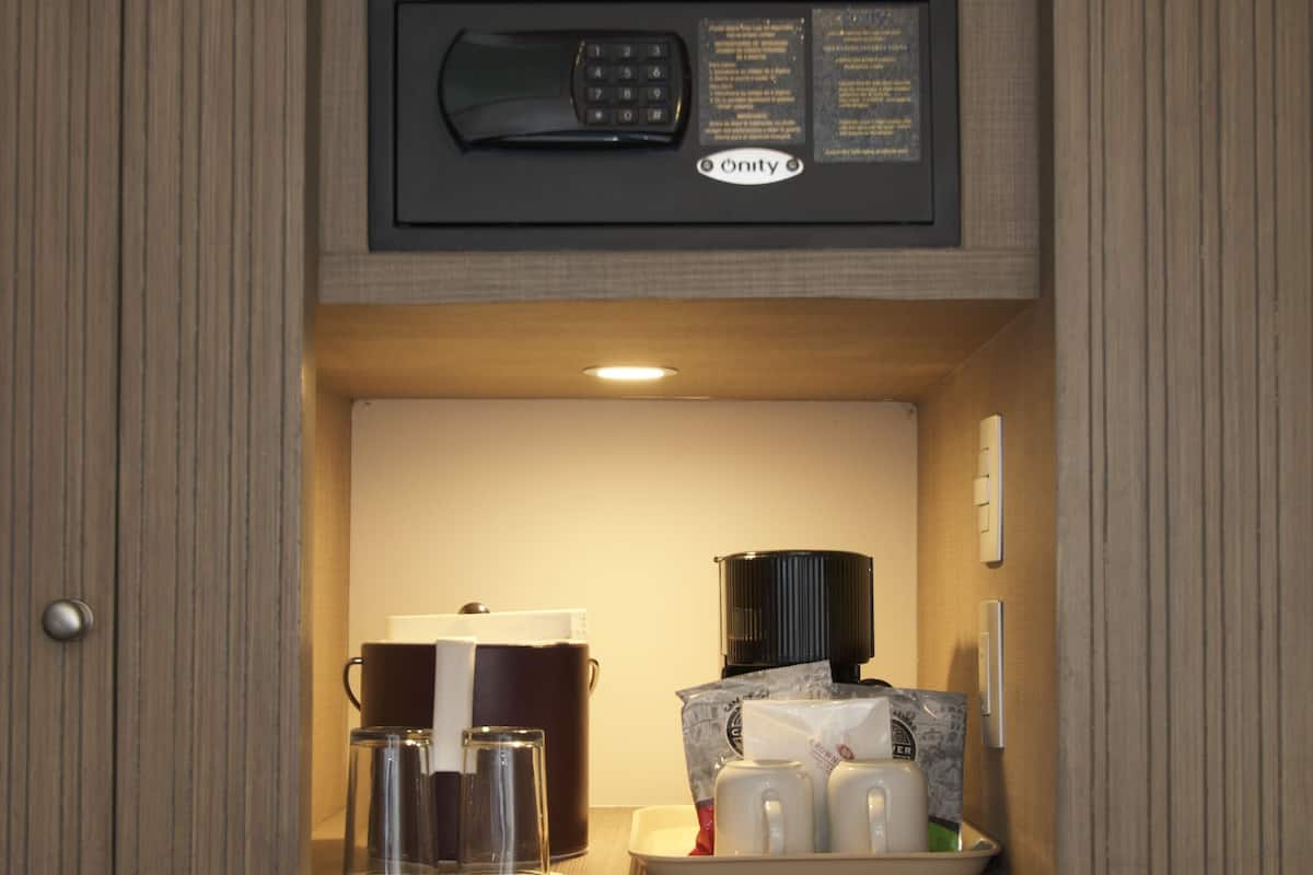 Una kitchenette compacta con cafetera integrada, microondas y pequeño espacio para café con tazas y hervidor.