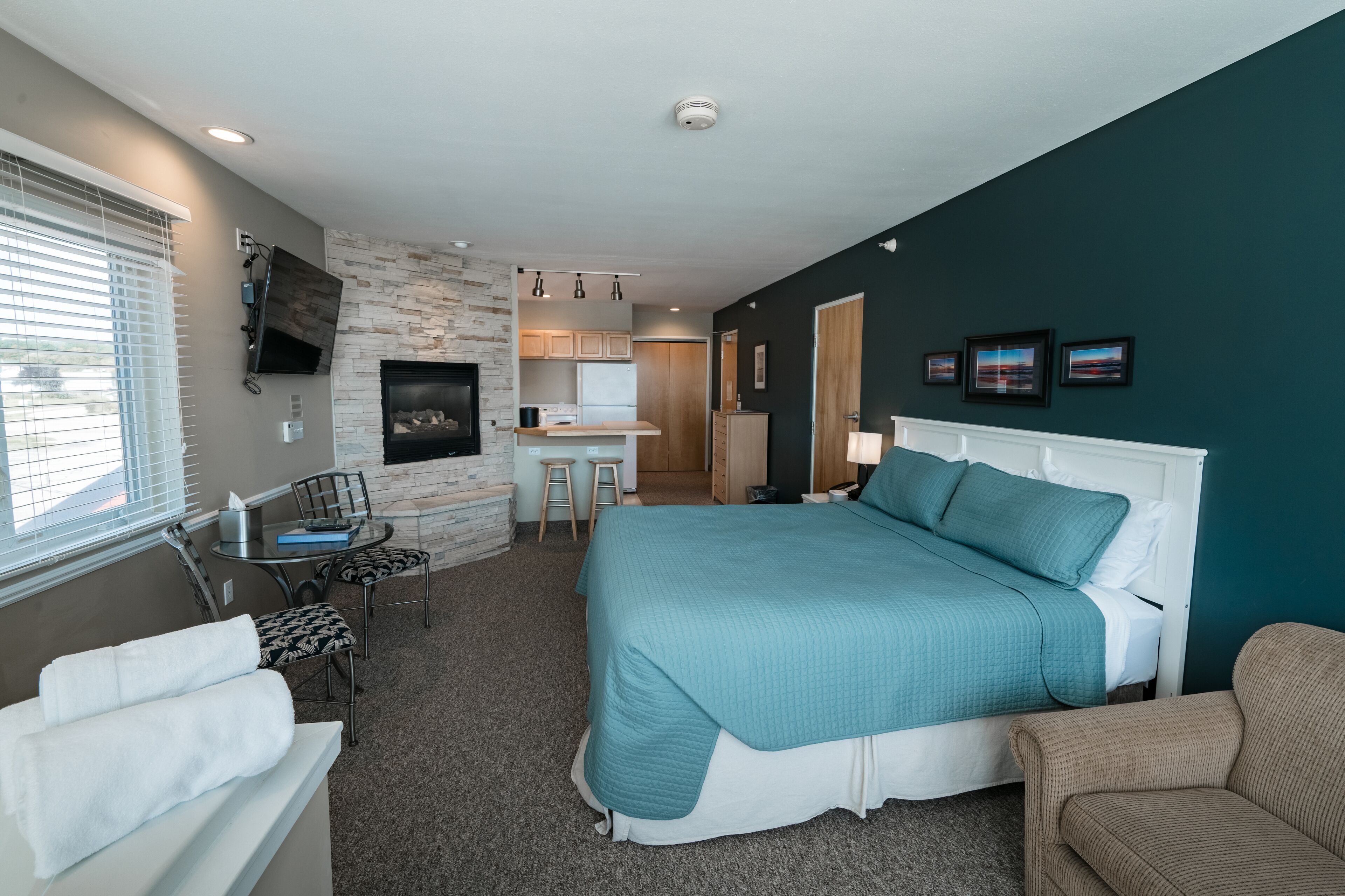 A bedroom with a large bed, a desk, and a kitchenette.
