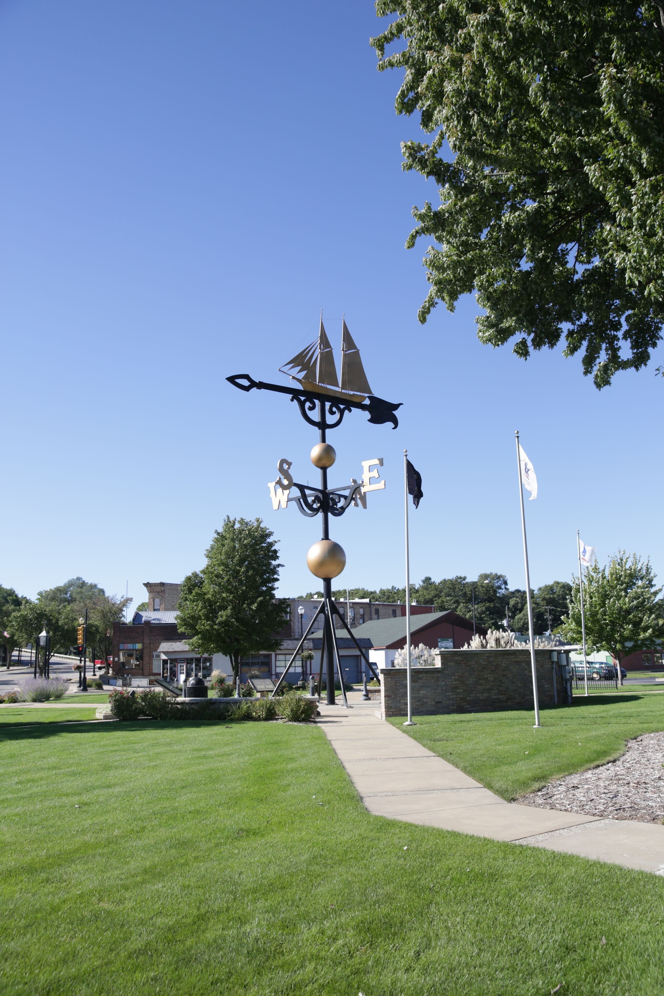 A weather vane sculpture with directional indicators, a paved walkway, and a building in the background.