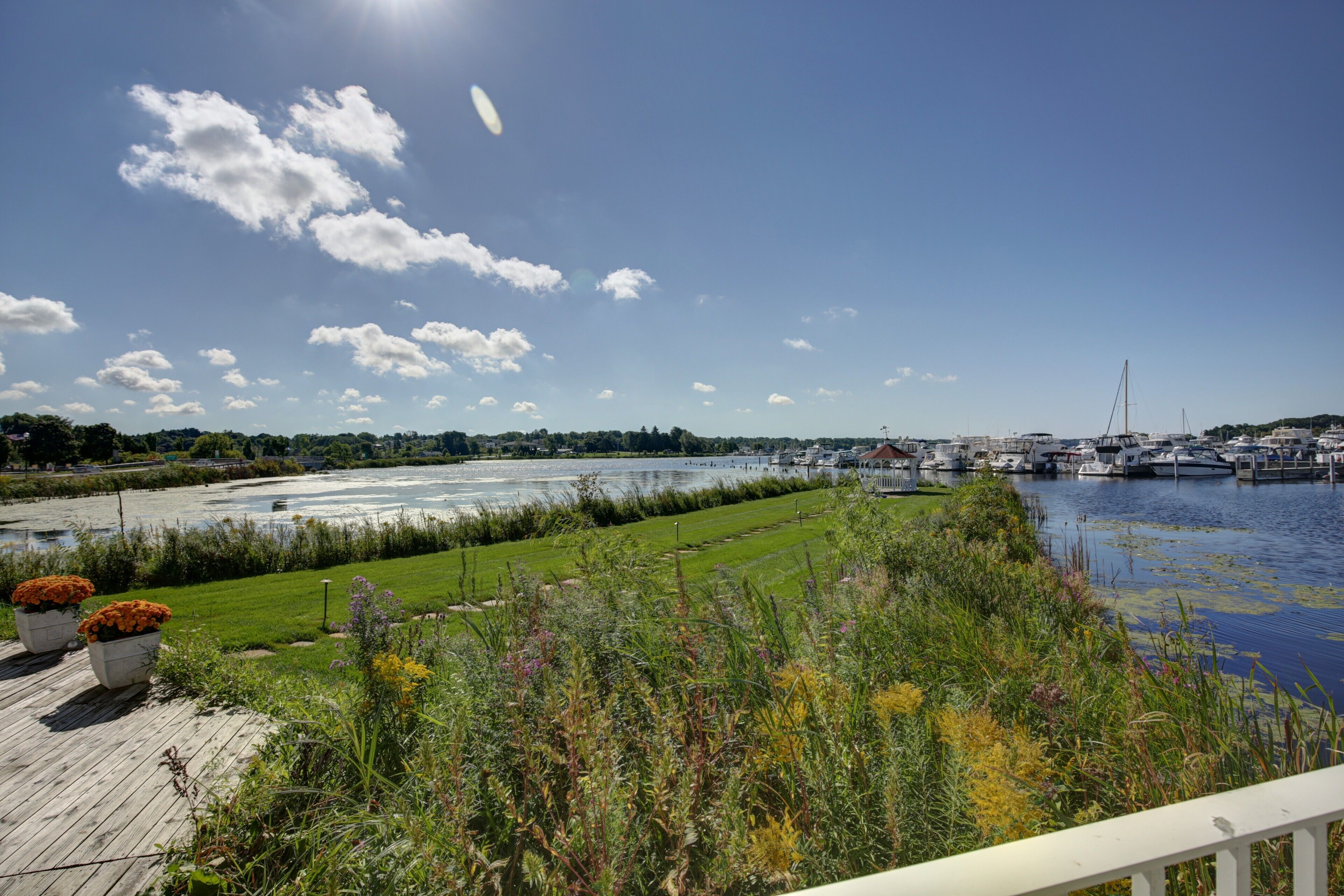 A riverside view with boats docked, grassy areas, and a clear sky.