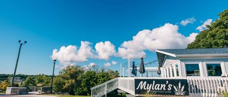 Un restaurante junto al agua llamado "Mylan's", con fachada blanca, una zona de estar cubierta al aire libre y una escalera que conduce a la entrada.