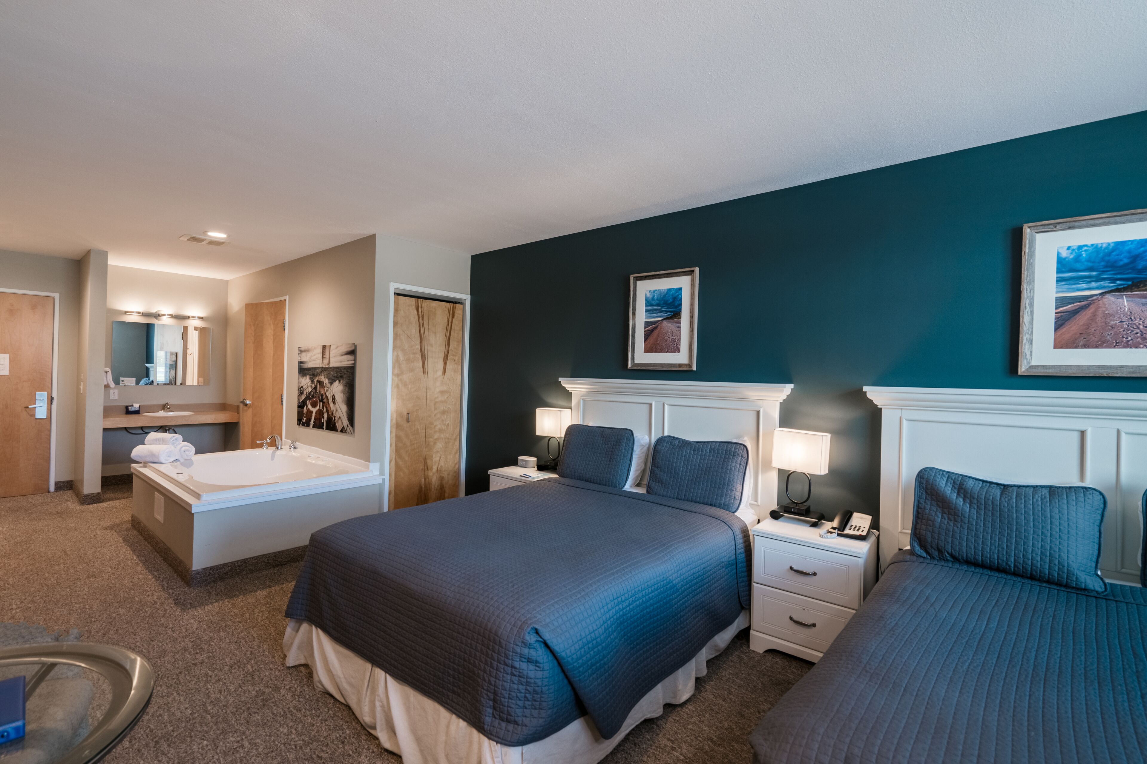 Una habitación de hotel con una cama grande, baño privado con bañera y un pequeño escritorio con lámpara.