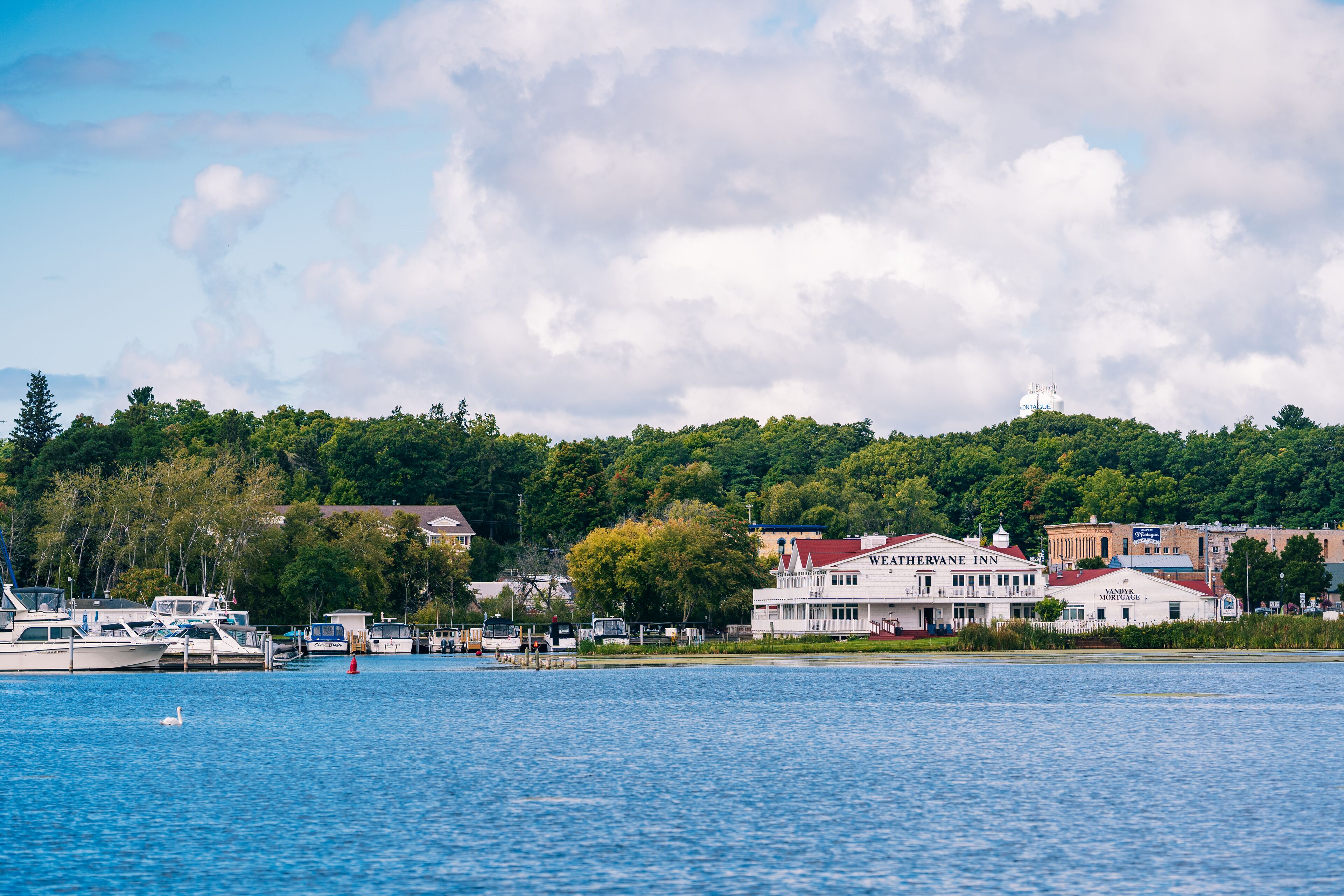 A waterfront hotel with a dock, boats, and a forested hillside in the background.