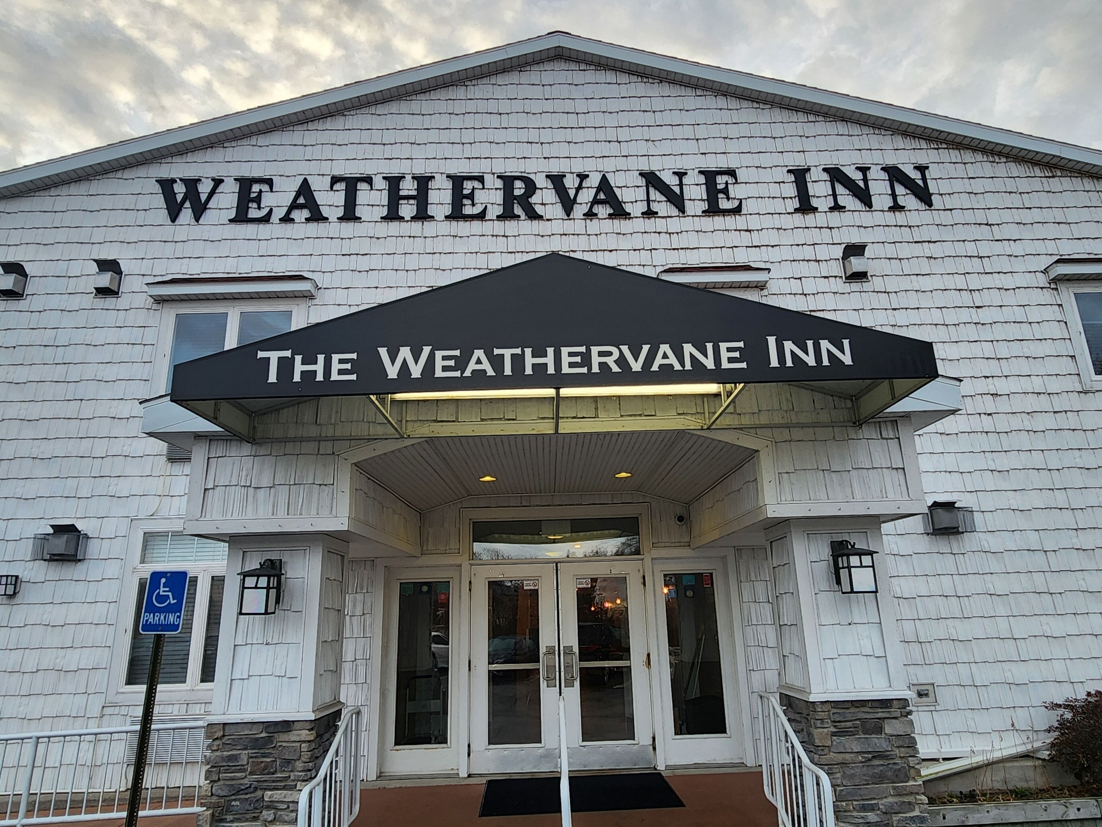 The exterior of The WeatherVane Inn, featuring a prominent entrance with a black awning and a handicap parking sign.