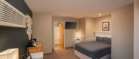 Quarto de hotel com cama, escrivaninha com luminária, televisão na parede e porta que dá para outro cômodo.