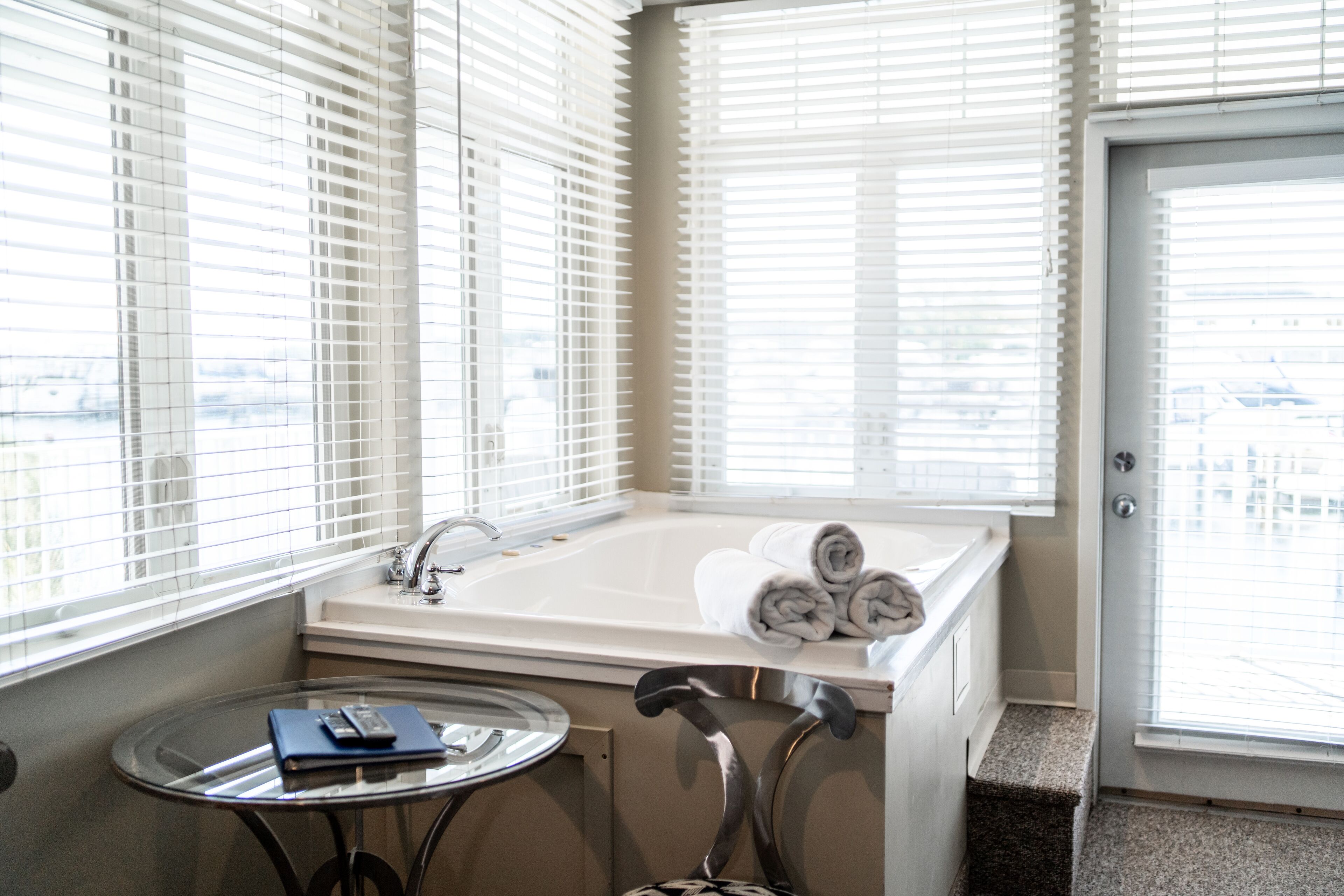 A bathroom with a bathtub, a sink, and a small table with a book and remote control.