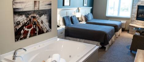 A hotel room with a large bathtub, two beds, a desk, and a fireplace.