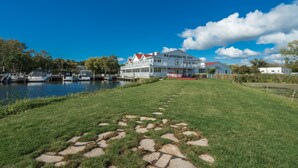 A large white building with a red roof, labeled "WEATHERVANE INN," situated by a body of water with boats docked nearby. - The Weathervane Inn (Montague)
