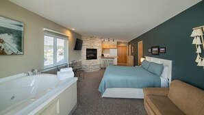 A bedroom with a large bed, a separate bathroom with a bathtub, a kitchenette, and a stone accent wall. - The Weathervane Inn (Montague)