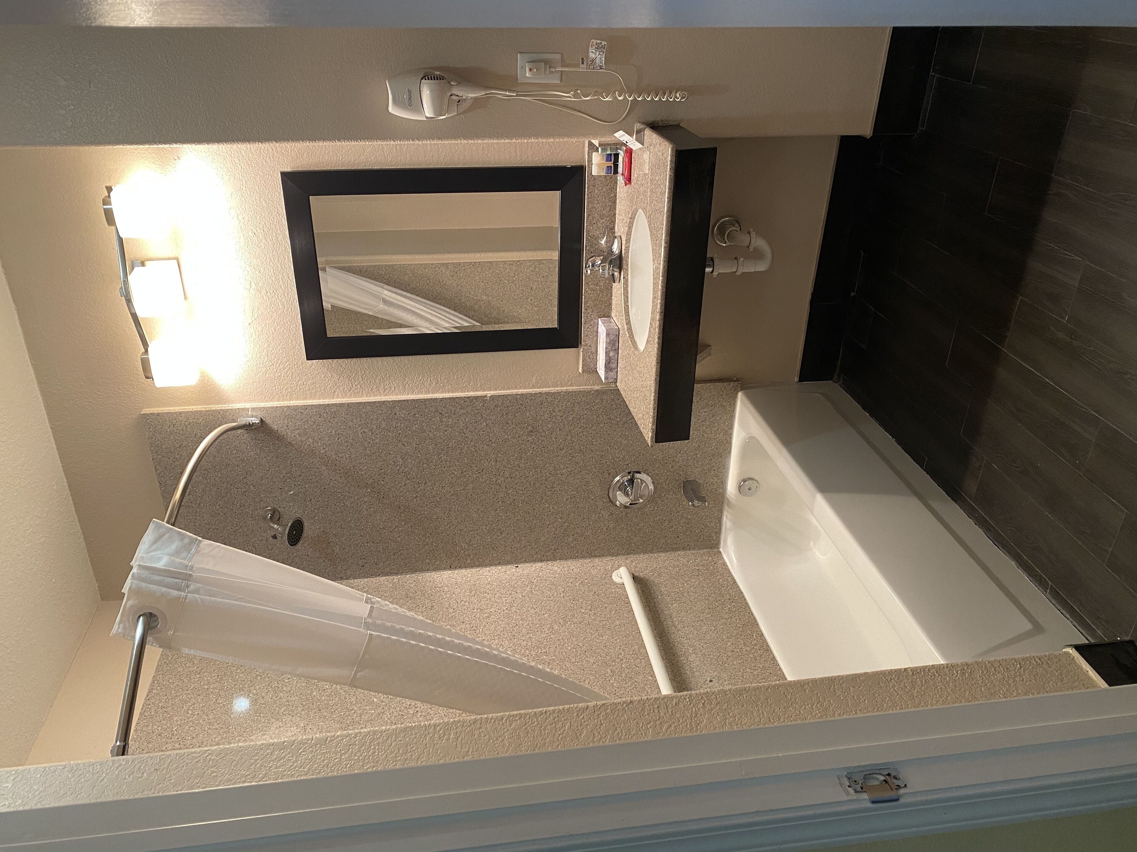 A bathroom with a bathtub, a shower, a sink, a mirror, and a hairdryer on the wall.