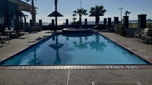 A pool area with lounge chairs, a hot tub, and a view of the ocean.