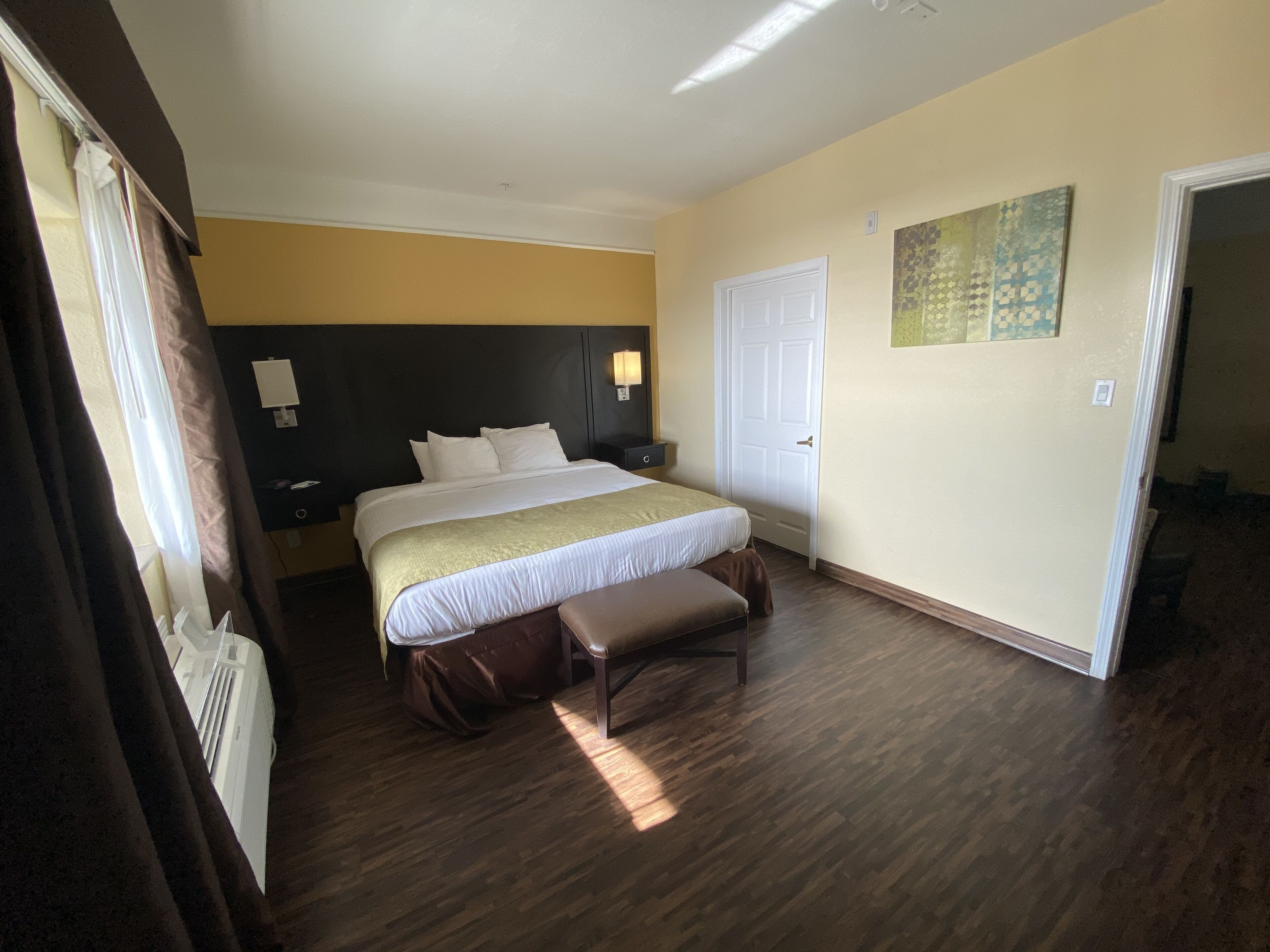 A hotel room with a large bed, a bench, a door, and a painting on the wall.