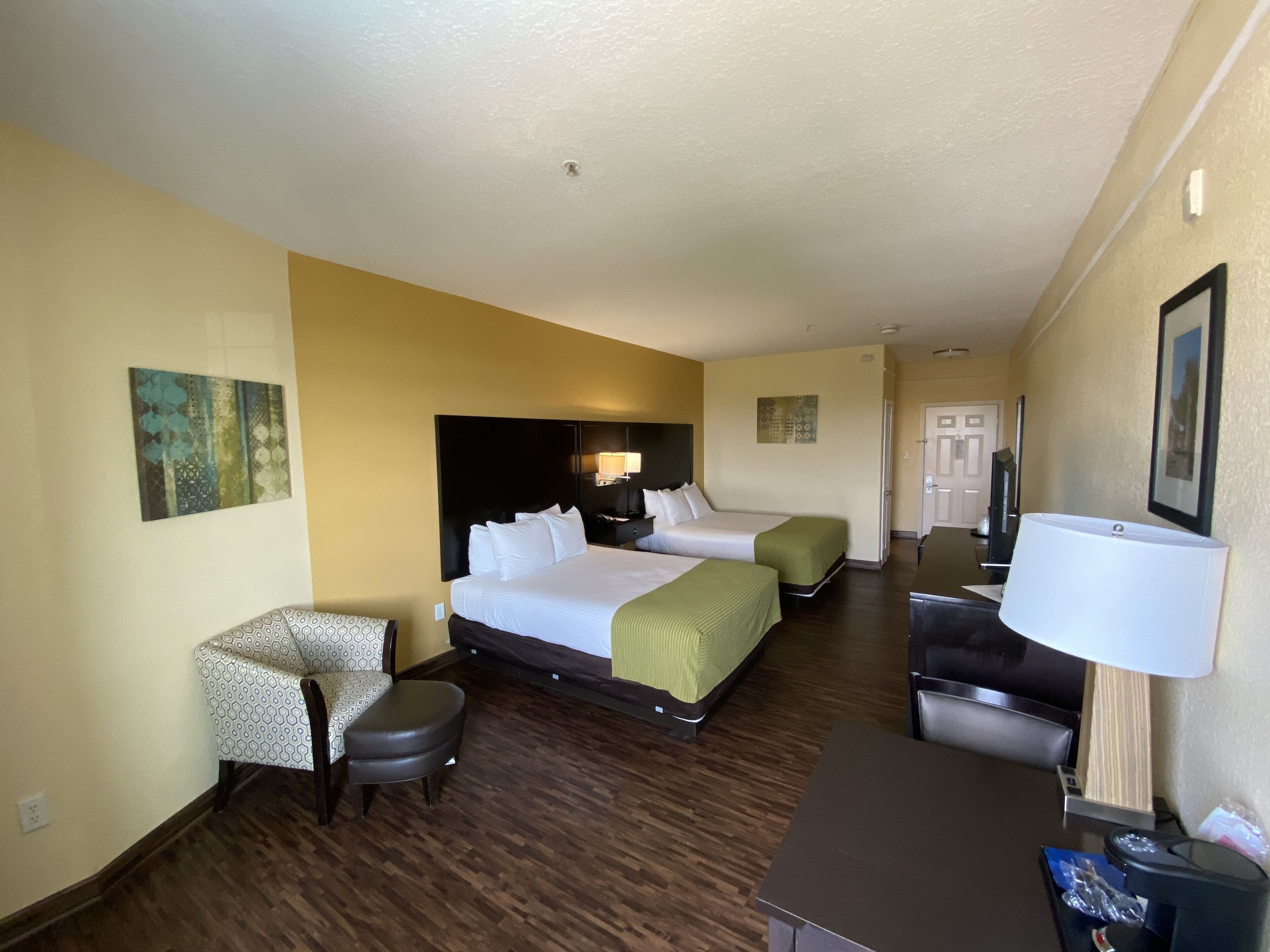 Une chambre d’hôtel avec deux lits, un bureau, une chaise et une lampe.