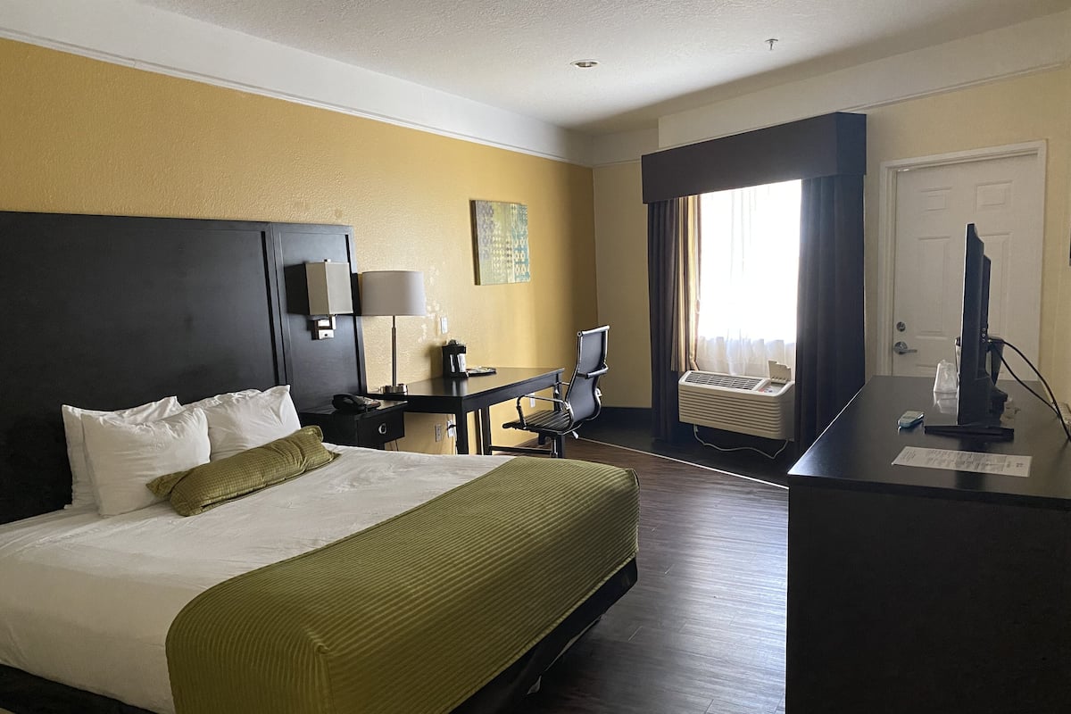 A hotel room with a bed, desk, chair, and a window with curtains.