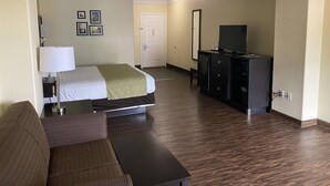 A hotel room with a bed, a desk, a dresser, and a television.