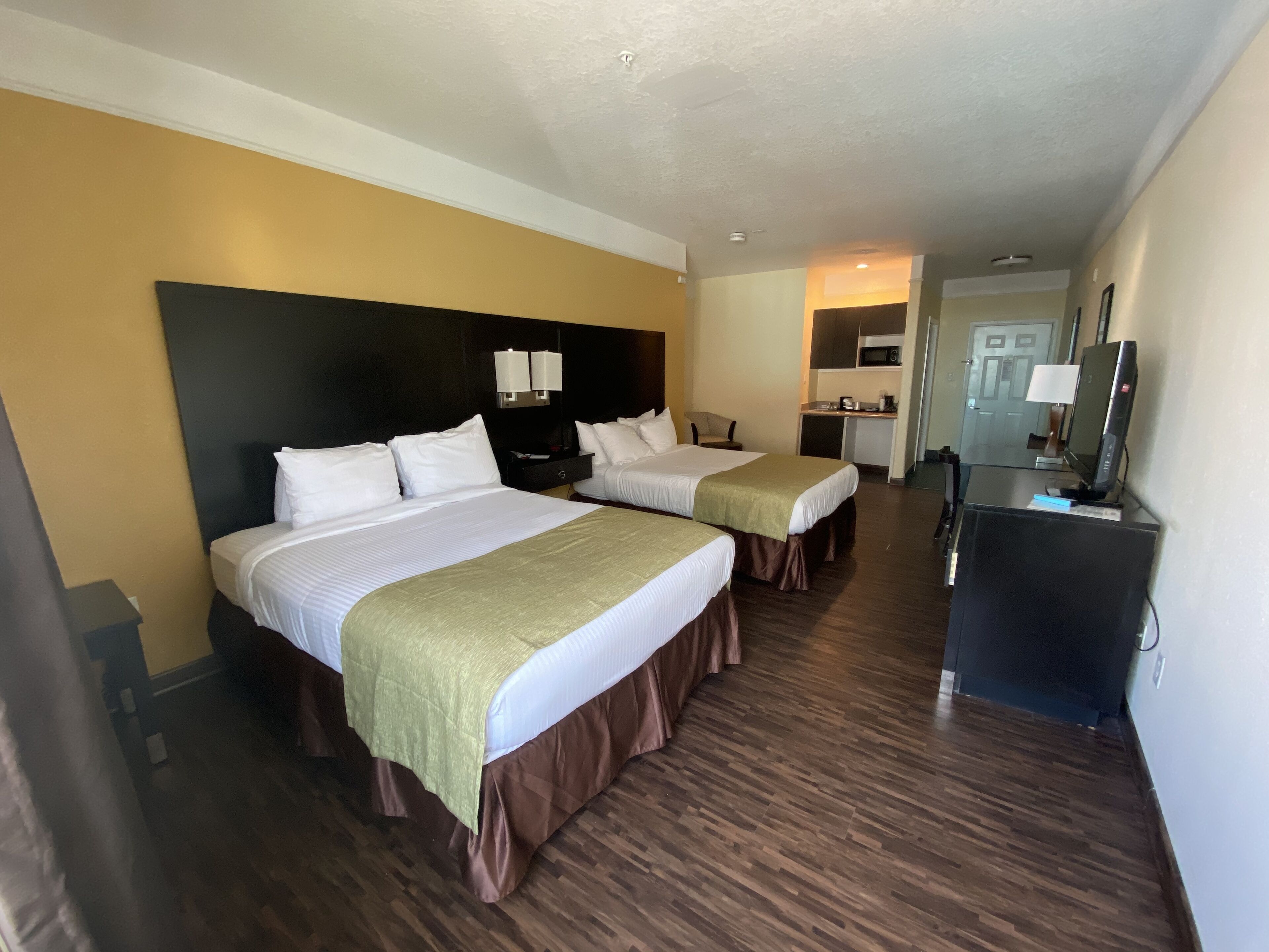 A hotel room with two beds, a desk, a television, and a kitchenette.