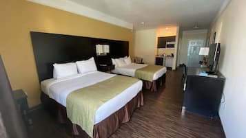A hotel room with two beds, a desk, a television, and a kitchenette.