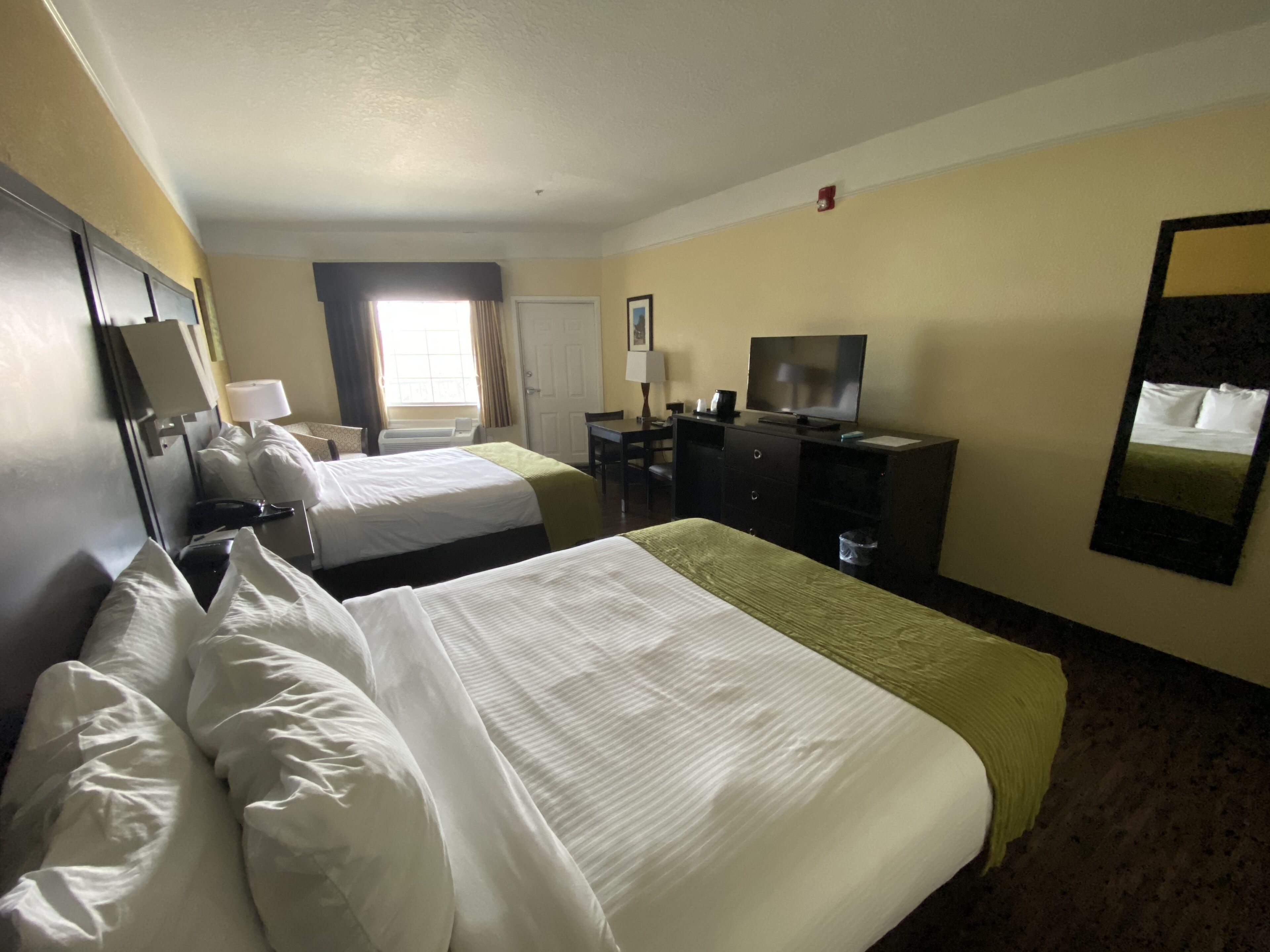 A hotel room with two beds, a desk, a television, and a mirror.