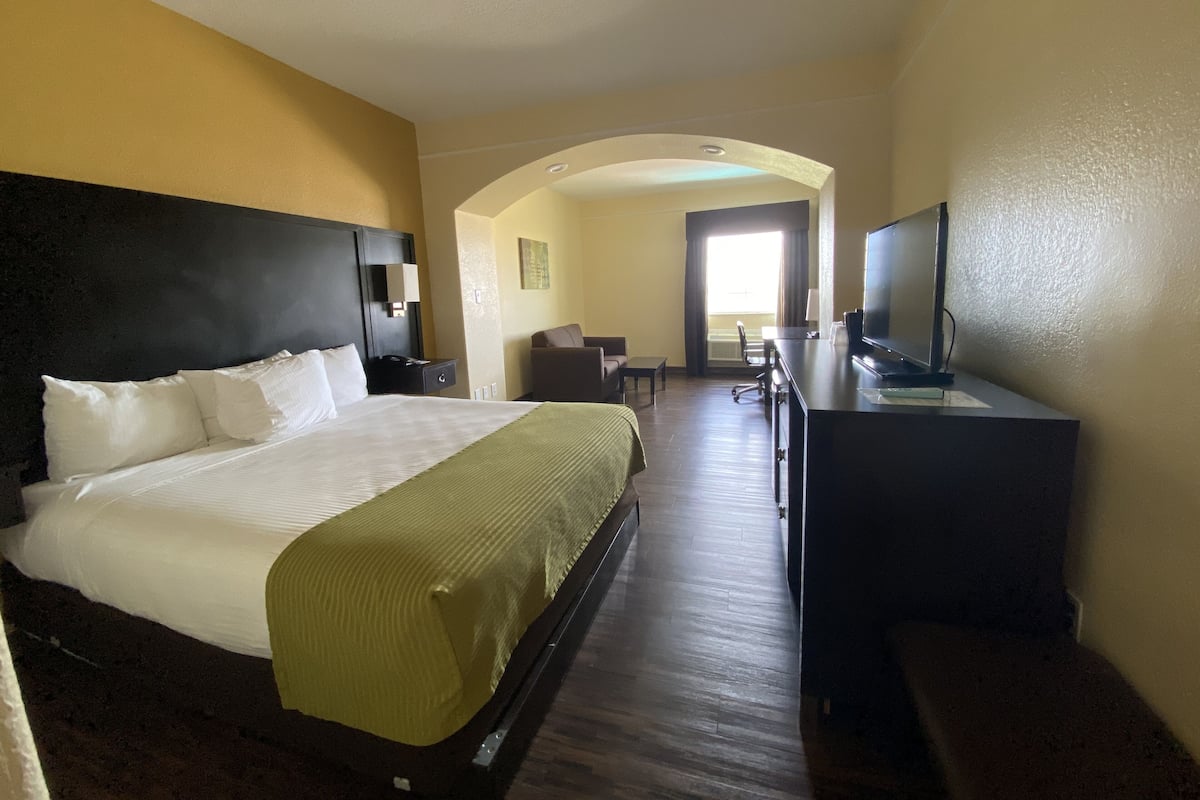 A hotel room with a large bed, a desk, a television, and an arched doorway leading to a balcony.