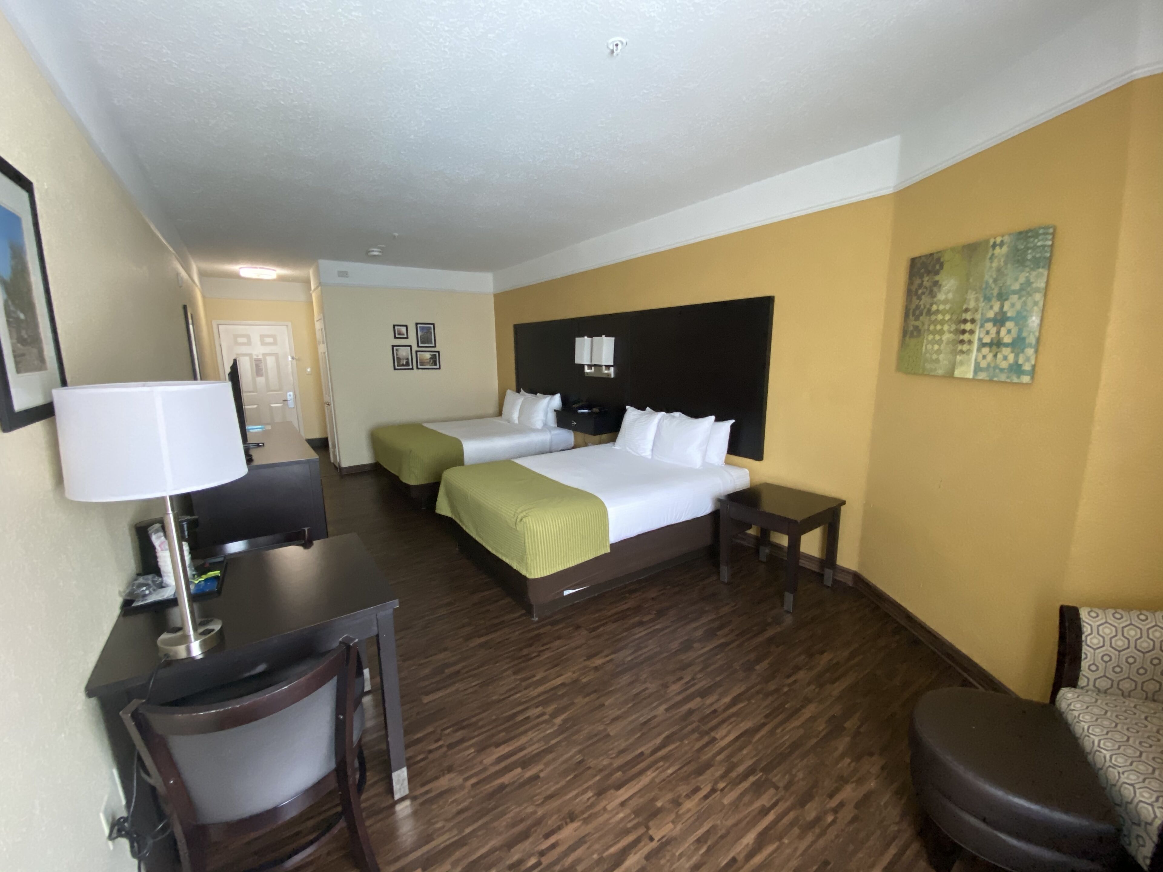 Habitación de hotel con dos camas, un escritorio, una silla, una lámpara y un cuadro en la pared.