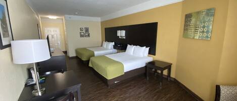 Habitación de hotel con dos camas, un escritorio, una silla, una lámpara y un cuadro en la pared.