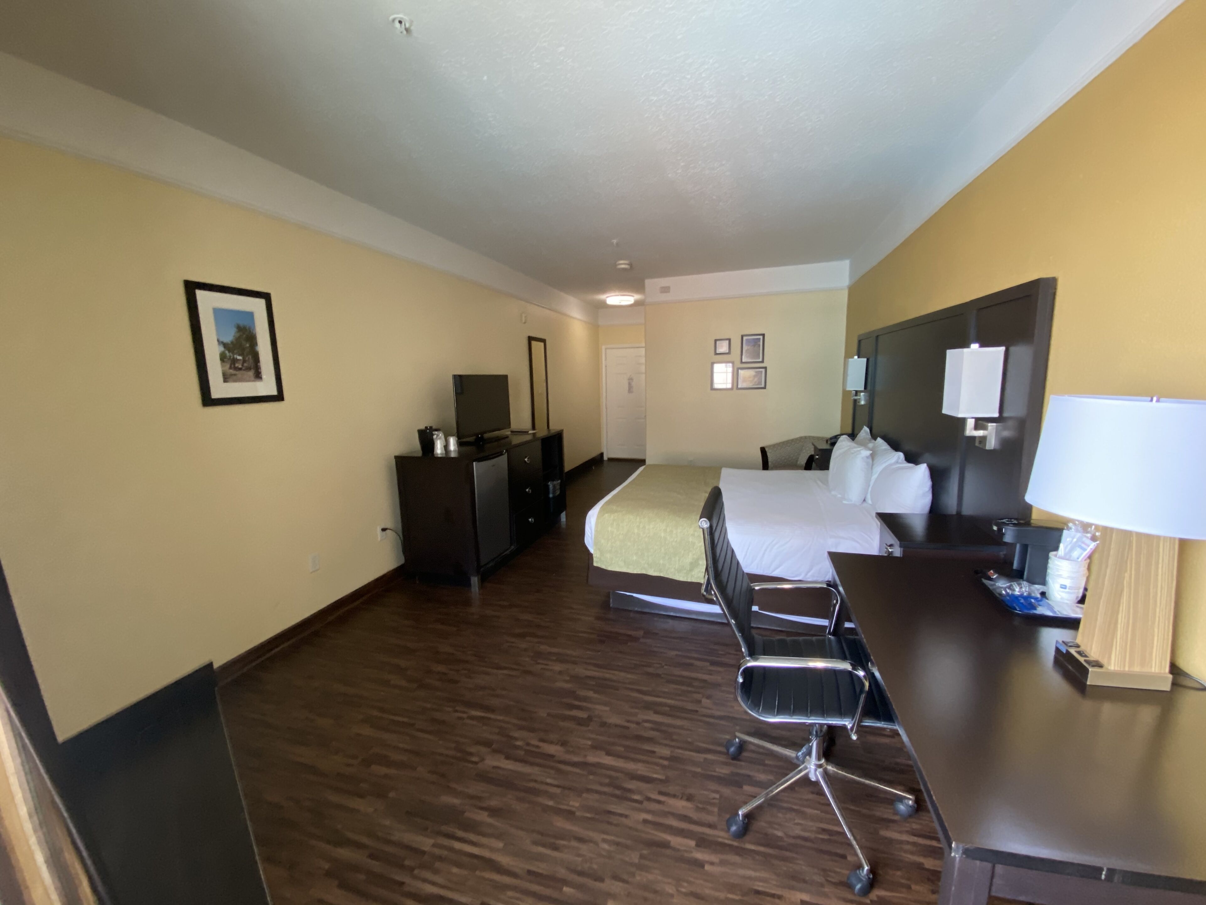 A hotel room with a bed, desk, chair, dresser, and a television.