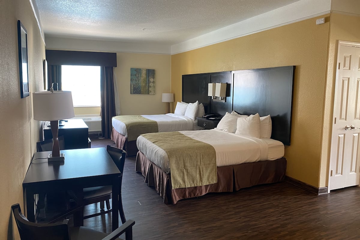 A hotel room with two beds, a desk, a chair, a lamp, a painting, and a door.