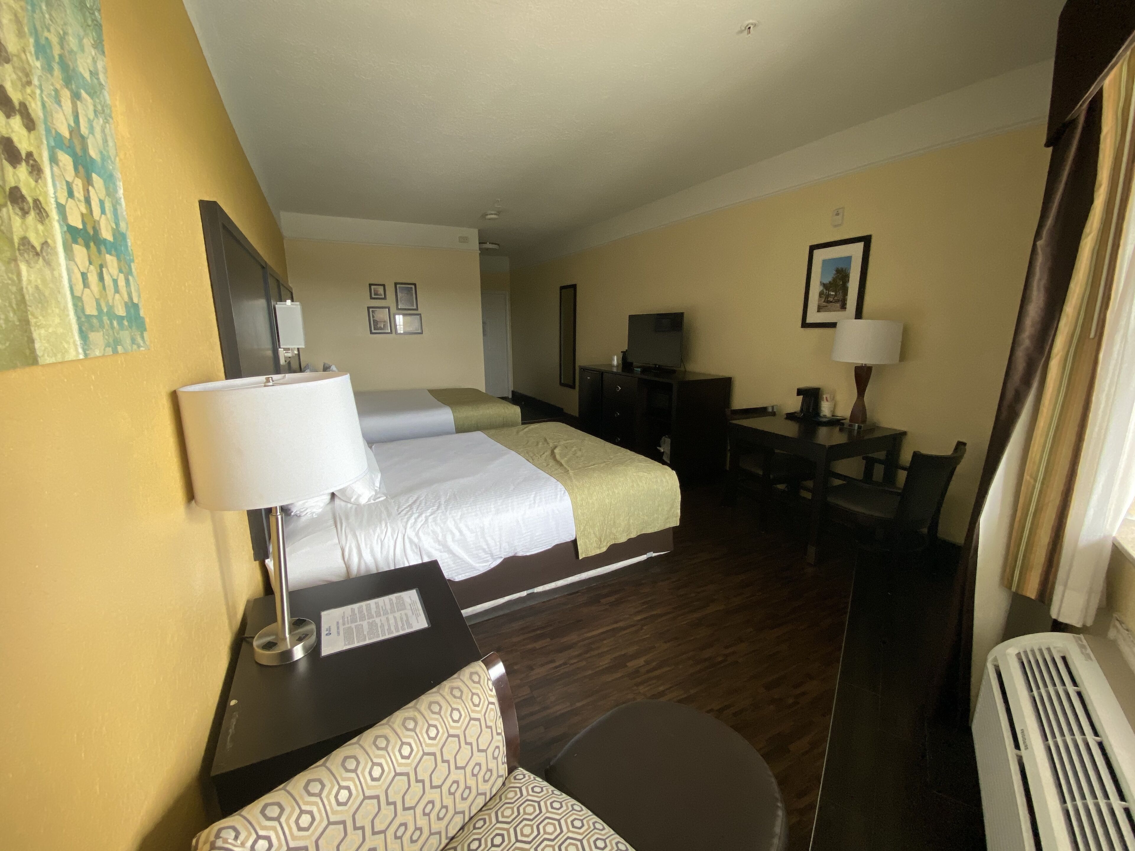 Quarto de hotel com duas camas, uma escrivaninha, uma cadeira, uma televisão e uma janela.