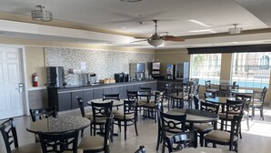 A spacious dining area with multiple tables and chairs, a kitchen area with modern appliances, and large windows providing natural light.