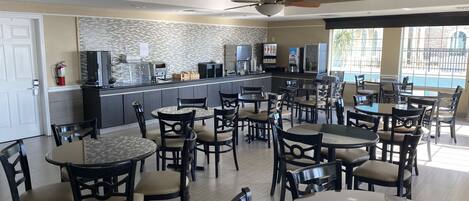 A spacious dining area with multiple tables and chairs, a kitchen area with modern appliances, and large windows providing natural light.