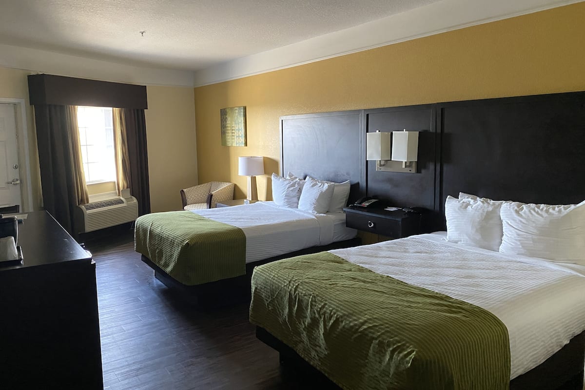 A hotel room with two beds, a desk, a chair, a lamp, and a painting on the wall.
