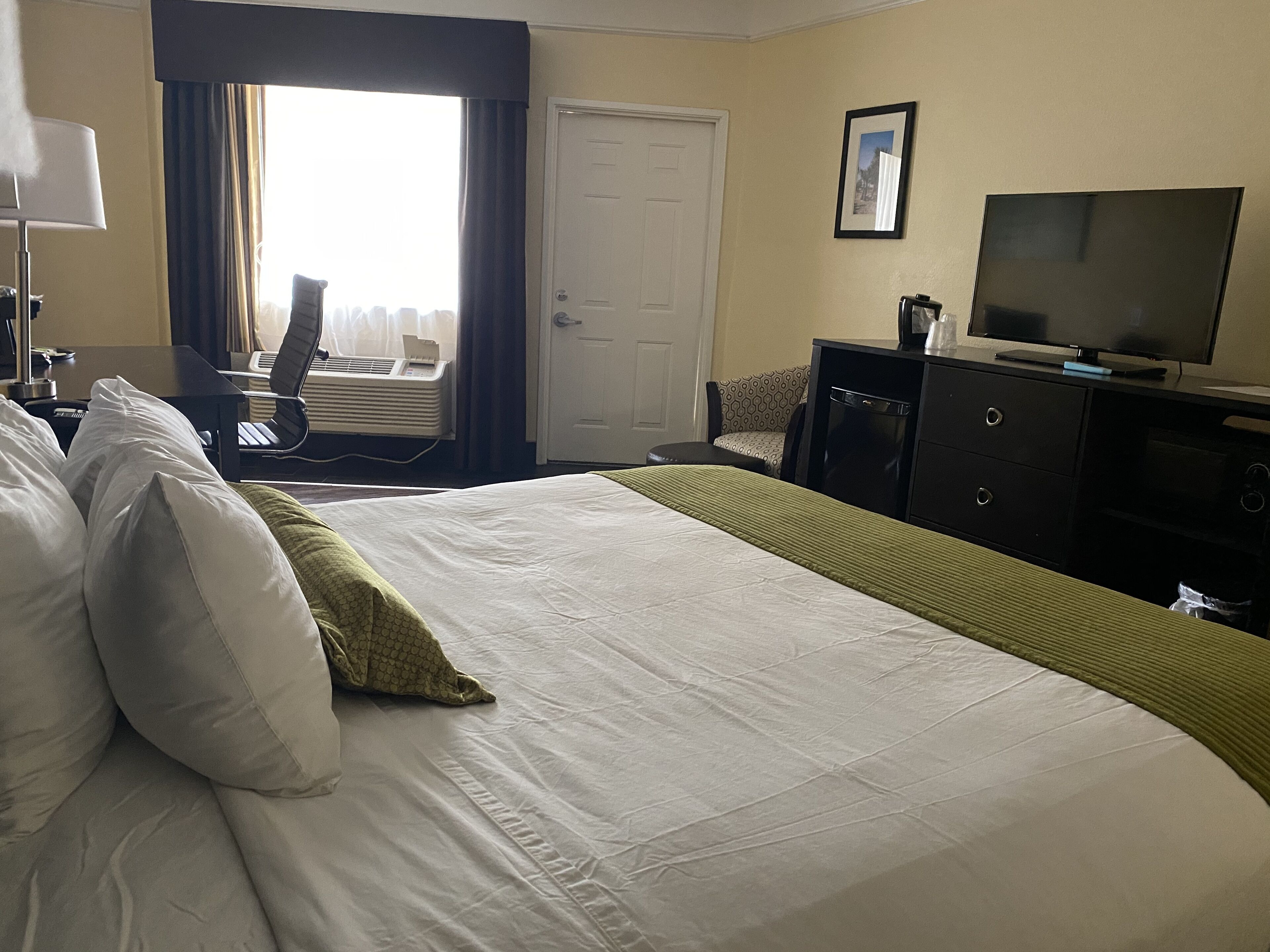 Une chambre d’hôtel avec un grand lit, une télévision, un bureau avec une chaise et une fenêtre avec des rideaux.