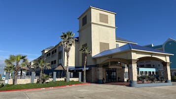 A hotel with a central tower, a covered entrance, and palm trees.