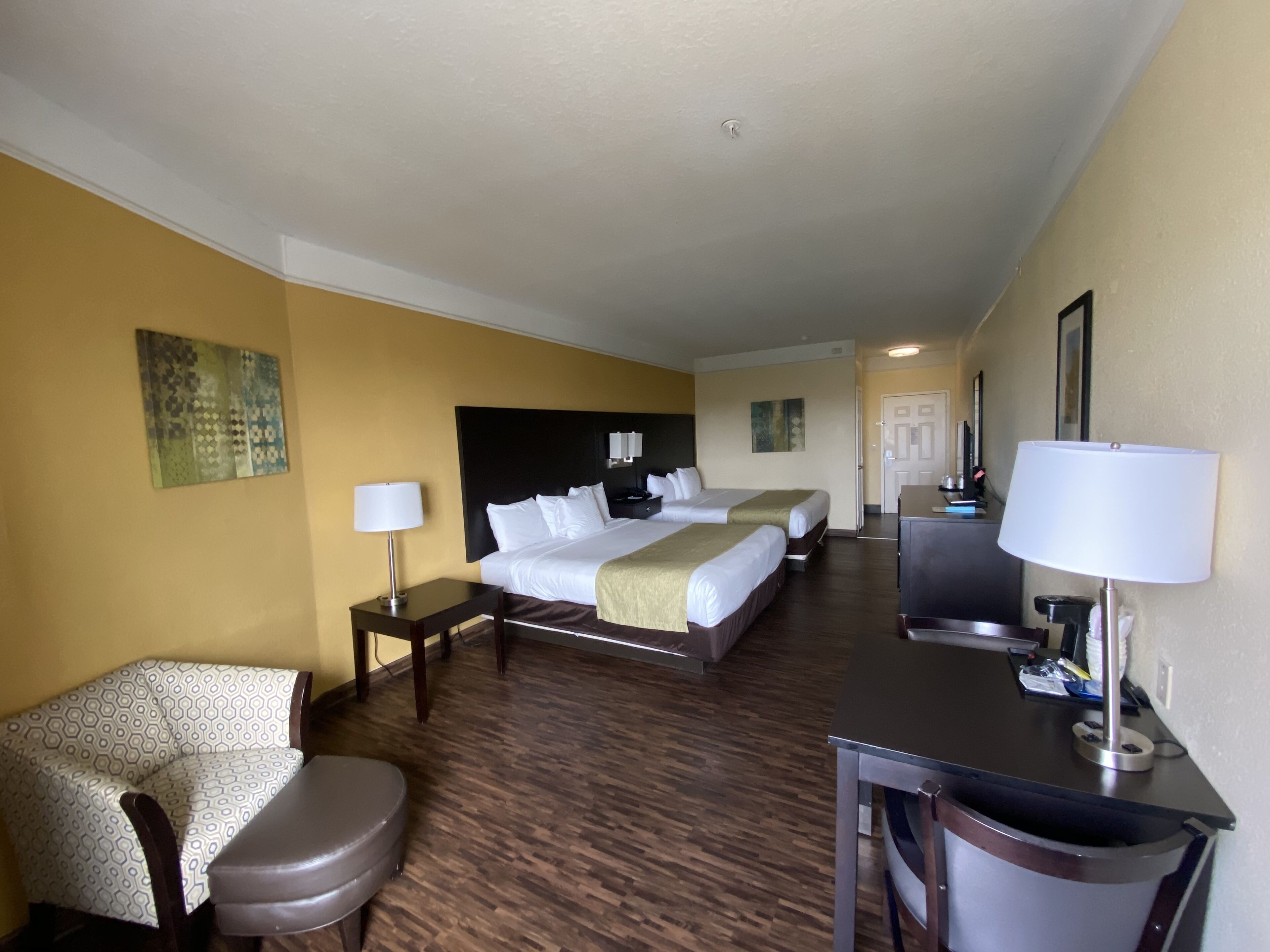 A hotel room with two beds, a desk, a chair, a lamp, and a painting on the wall.