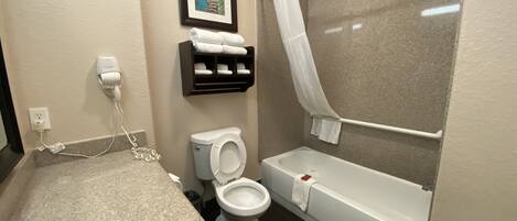 A bathroom with a toilet, sink, and bathtub. There is a towel rack with towels, a framed picture on the wall, and a power outlet with a hairdryer plugged in.