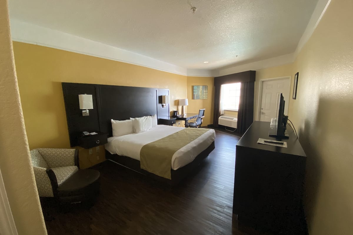 A hotel room with a large bed, a desk, a chair, a TV, and a window.