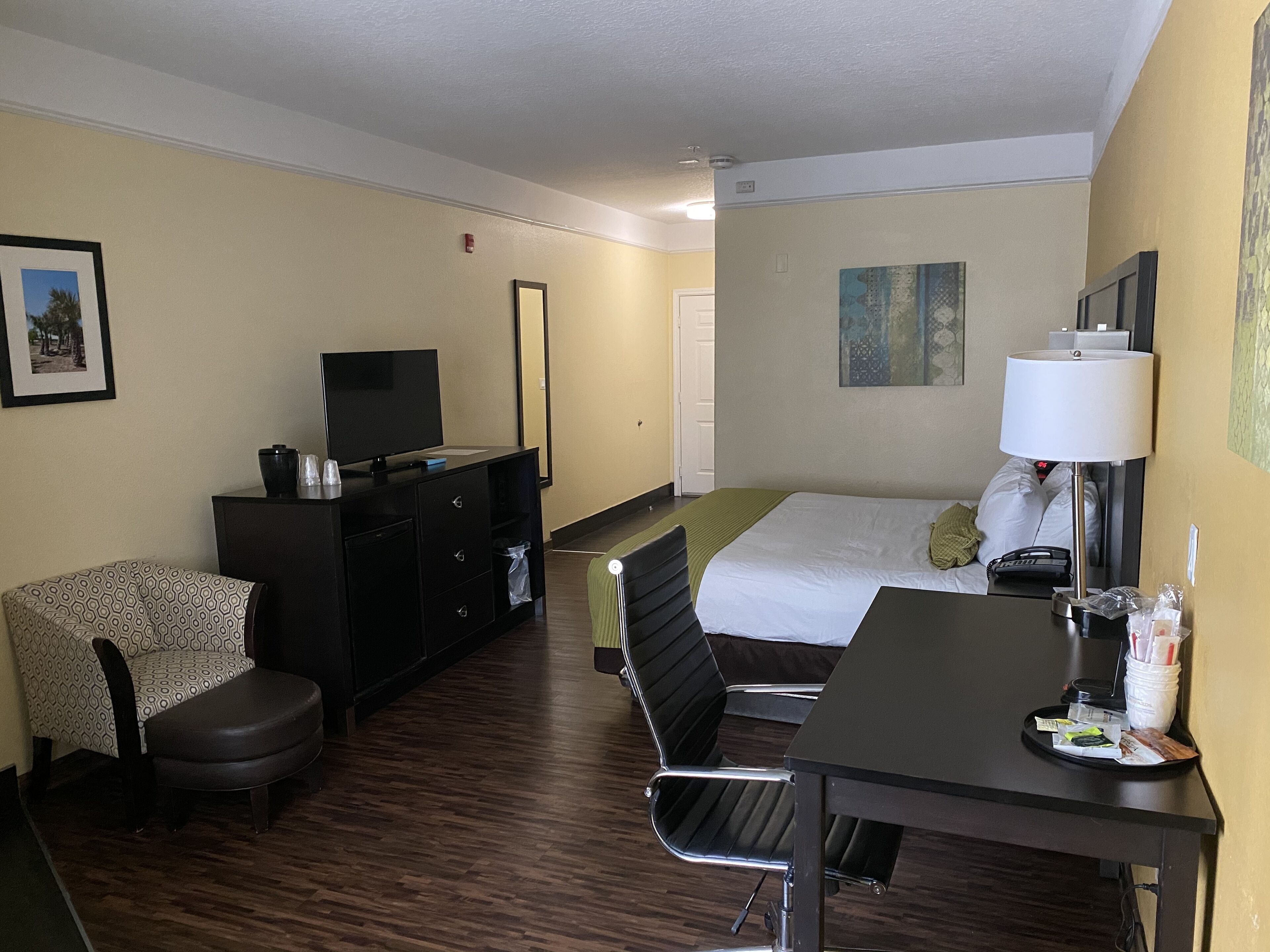 Quarto de hotel com cama, escrivaninha, cadeira, televisão, cômoda e abajur.