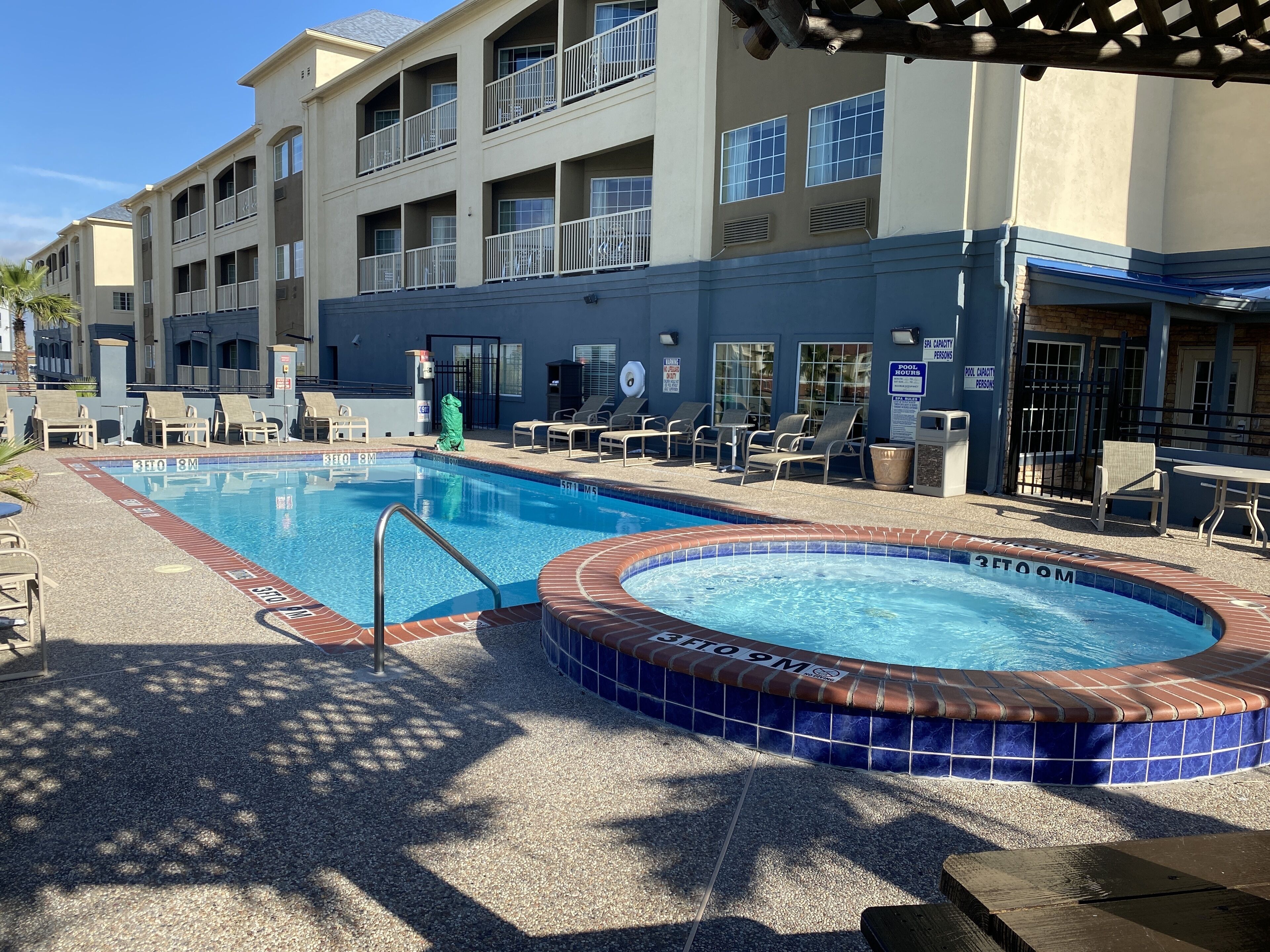 A swimming pool with a hot tub, lounge chairs, and a covered seating area.