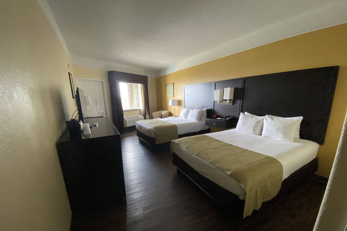 A hotel room with two beds, a desk, a chair, a nightstand, and a window with curtains.