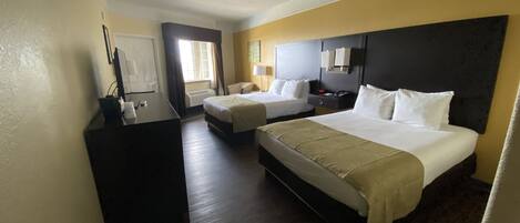 Hotelkamer met twee bedden, een bureau, een stoel, een nachtkastje en een raam met gordijnen.