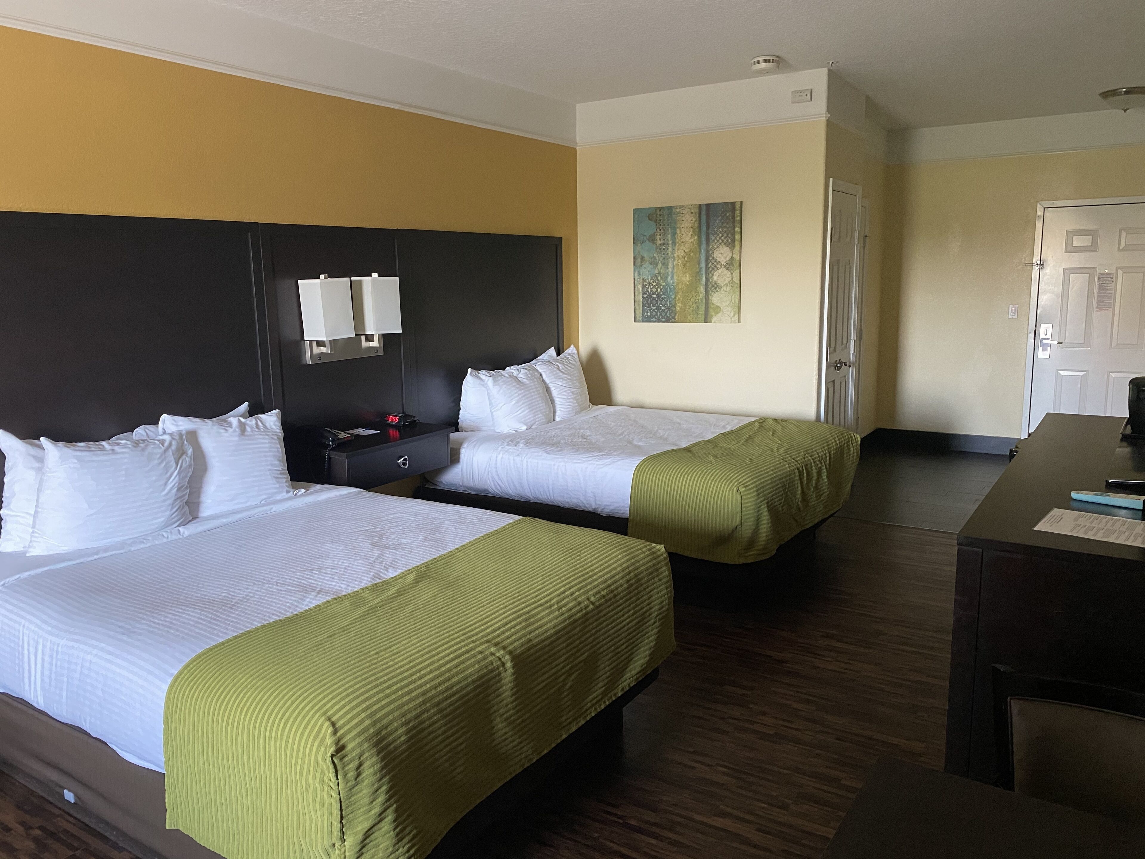 Une chambre d’hôtel avec deux lits, un bureau, une table de chevet et un tableau au mur.