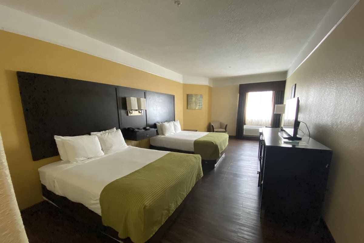 A hotel room with two beds, a desk, a chair, and a television.