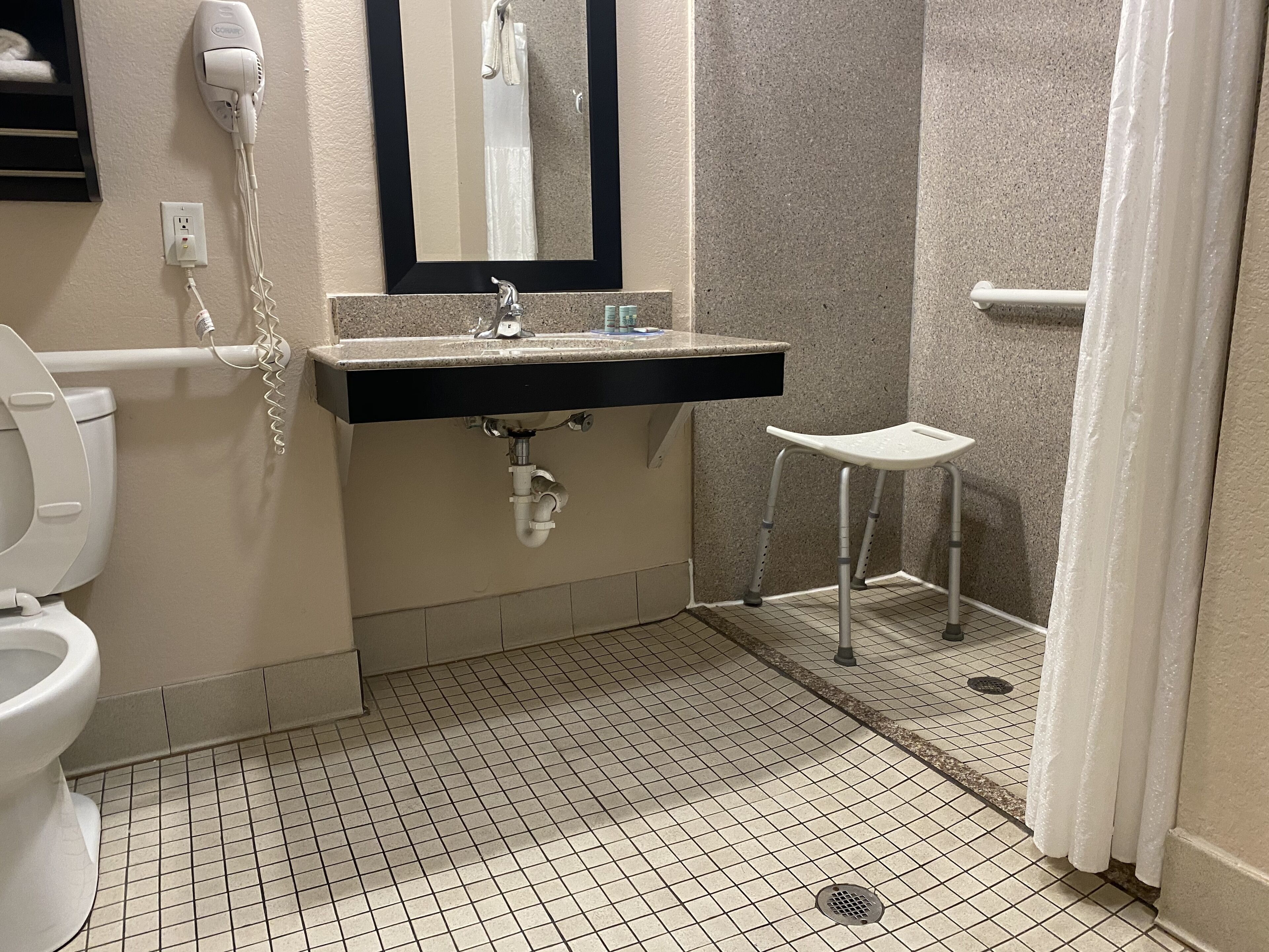 A bathroom with a toilet, sink, mirror, and a small stool.