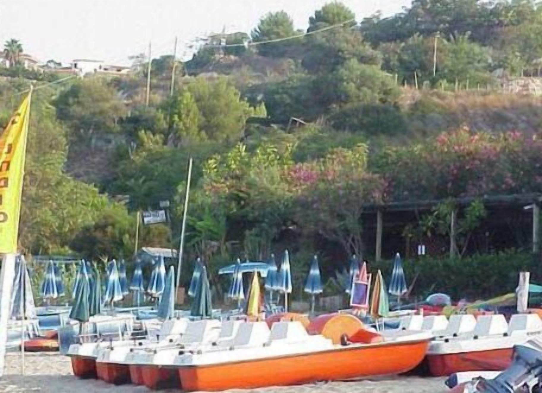 Una playa con varios barcos alineados, sombrillas y una bandera.
