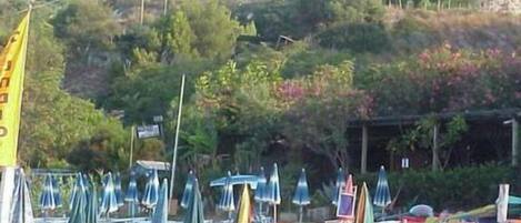 Una playa con varios barcos alineados, sombrillas y una bandera.
