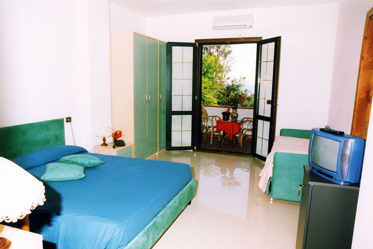 A bedroom with a bed, a television, and a view of an outdoor patio with a table and chairs.